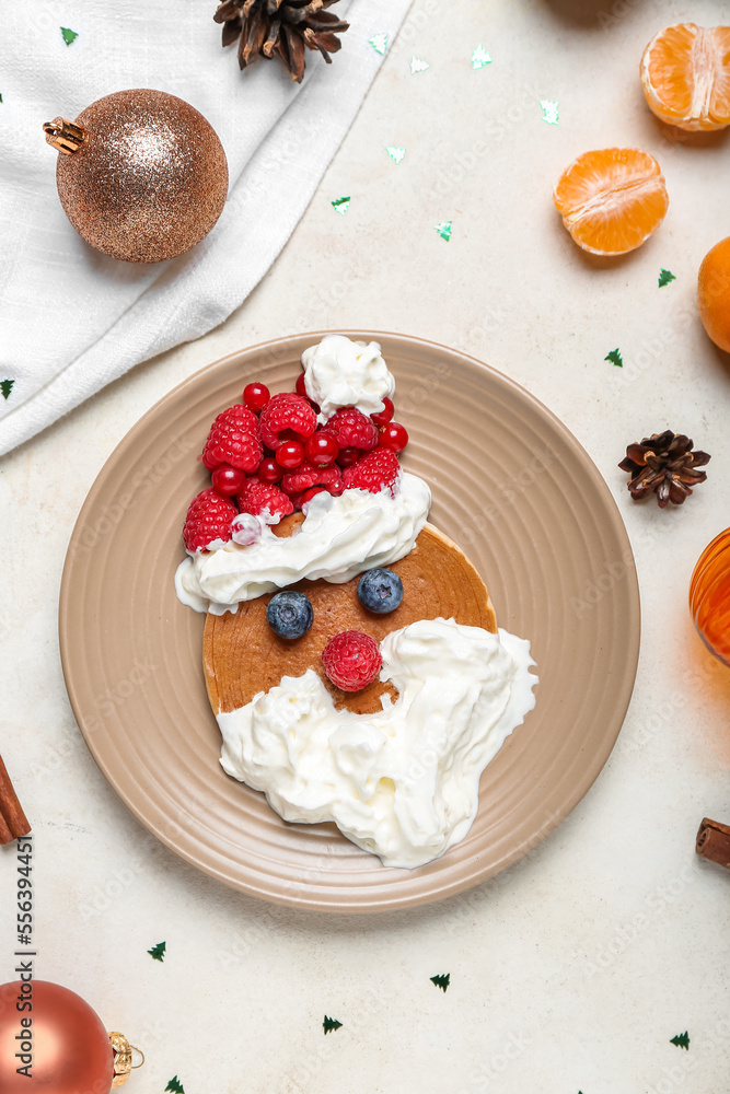 Plate with tasty Santa pancake and Christmas decor on light background