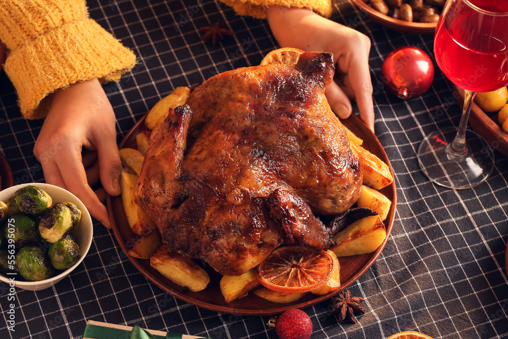 Woman with plate of Christmas chicken with potato on dining table at home, closeup