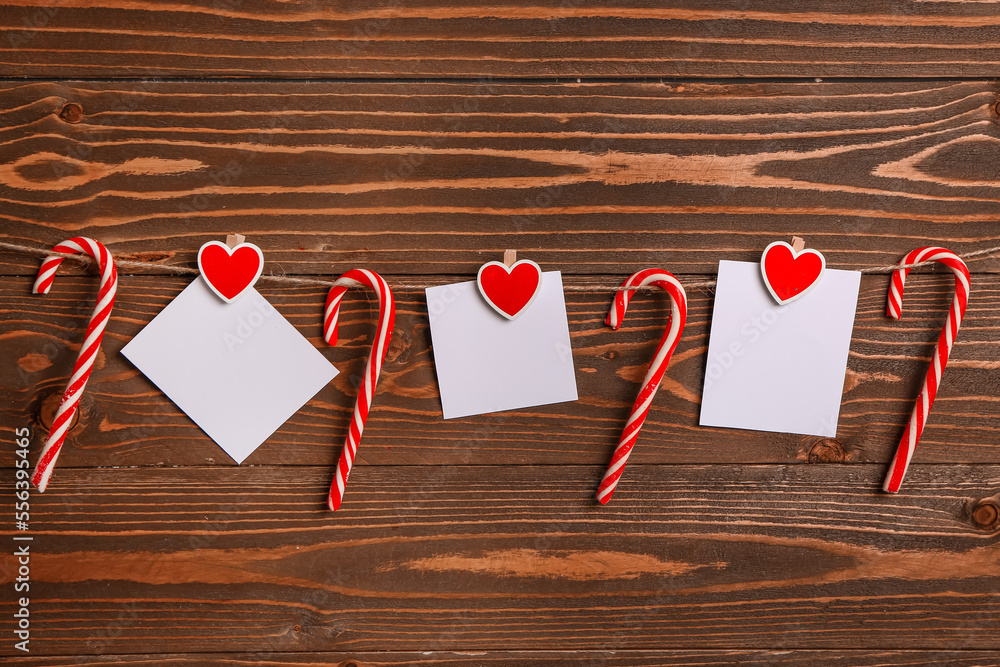 Sweet candy canes and blank sticky notes hanging on rope against wooden background