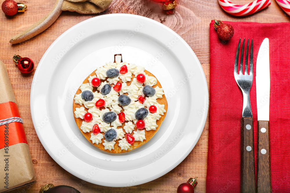 Plate with Christmas ball made of pancake, berries, whipped cream and decor on wooden table, closeup