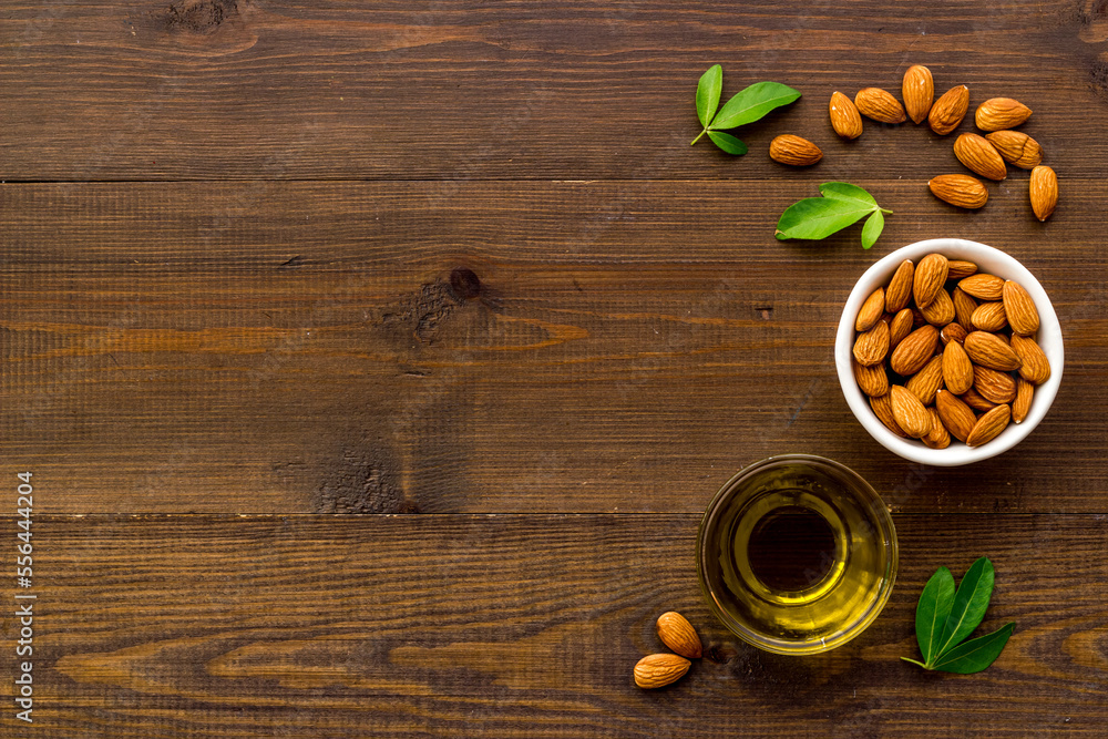 Sweet almond oil in glass jar and almond seeds with green leaf