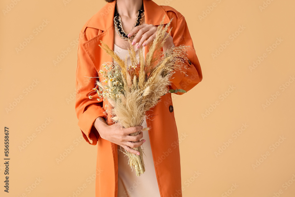 Fashionable woman with bouquet of dry flowers on color background