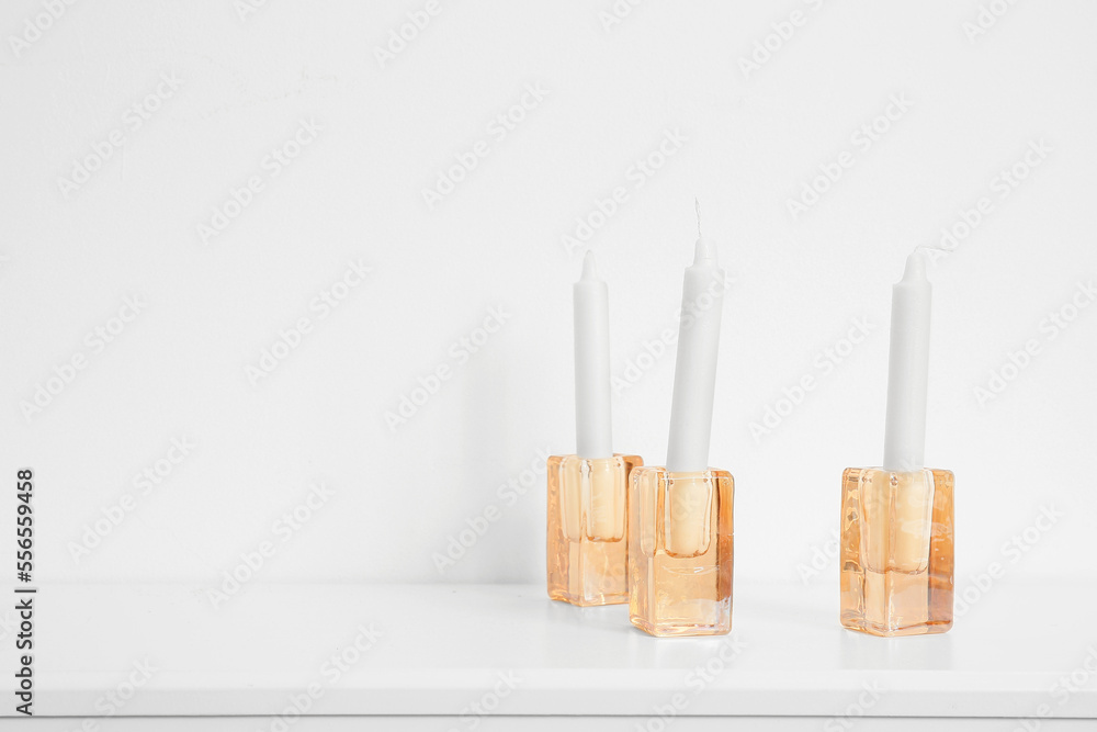 Holders with candles on shelf near white wall