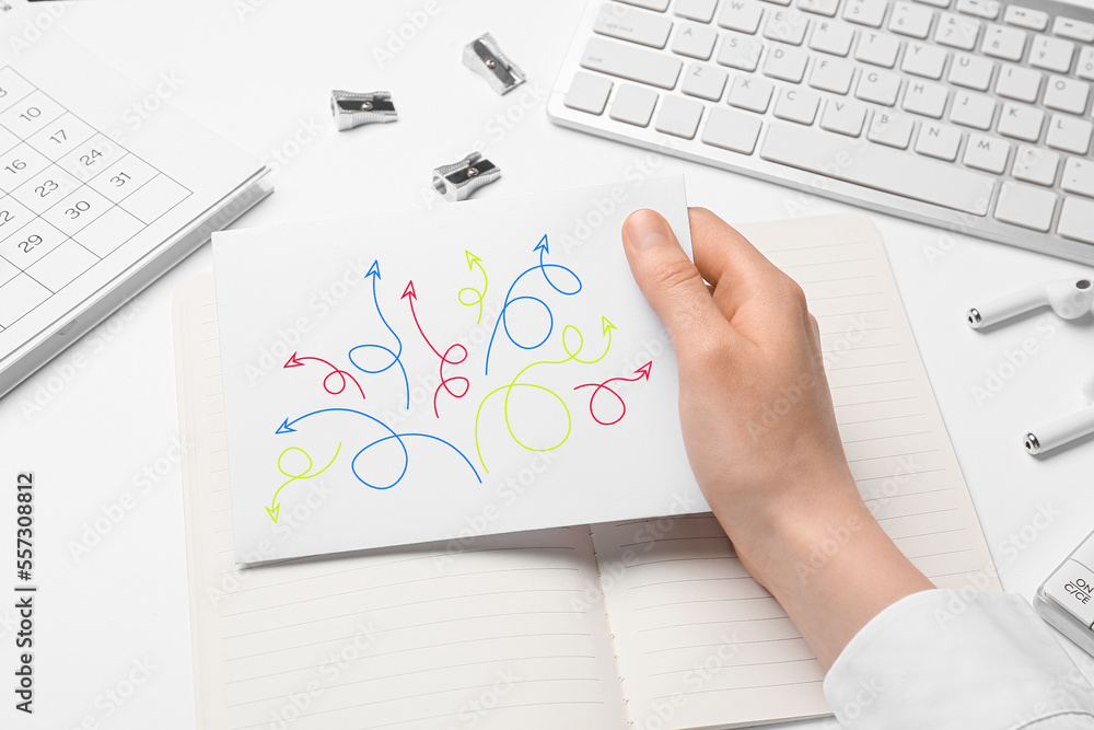 Woman holding paper sheet with drawn arrows at office table, closeup. Concept of choice