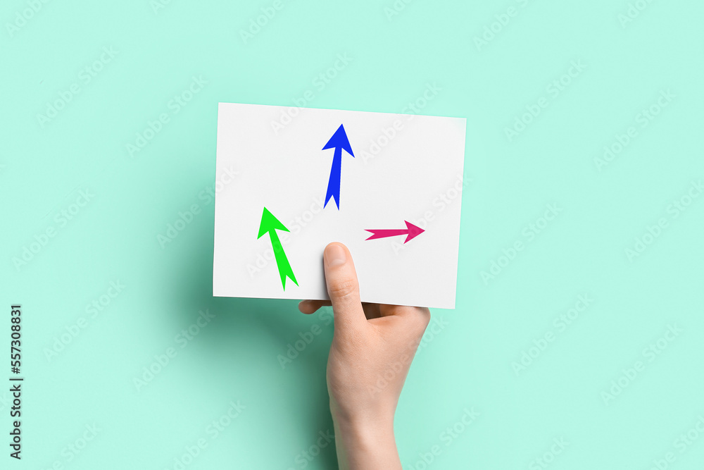 Hand holding paper sheet with drawn arrows on color background. Concept of choice