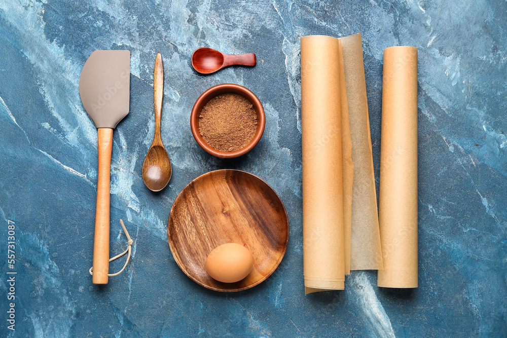 Rolls of baking paper and wooden kitchen utensils on blue background