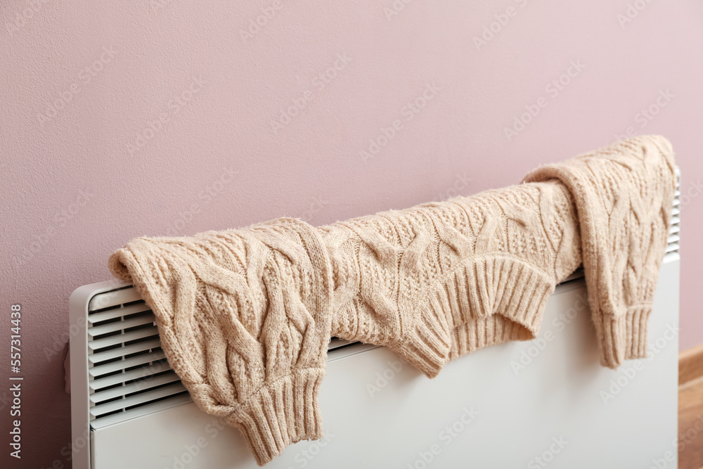 Warm sweater drying on electric radiator near pink wall, closeup