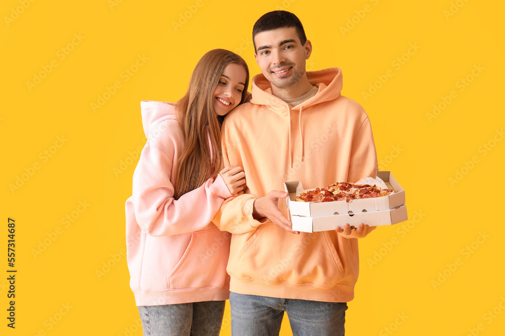 Happy young couple with fresh pizza on yellow background