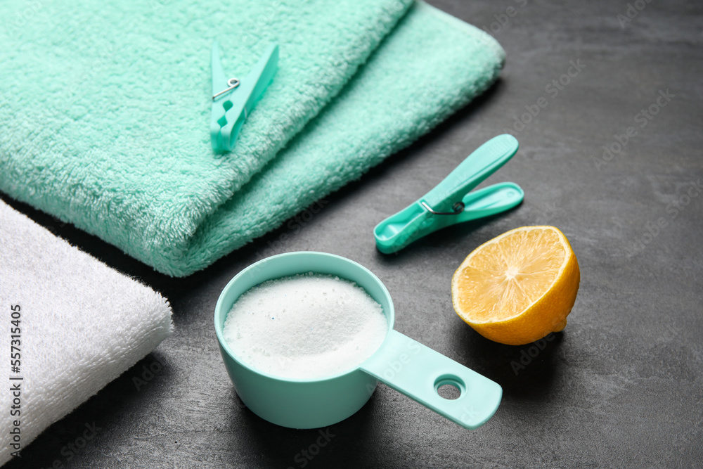 Scoop with laundry detergent, lemon and towels on black background