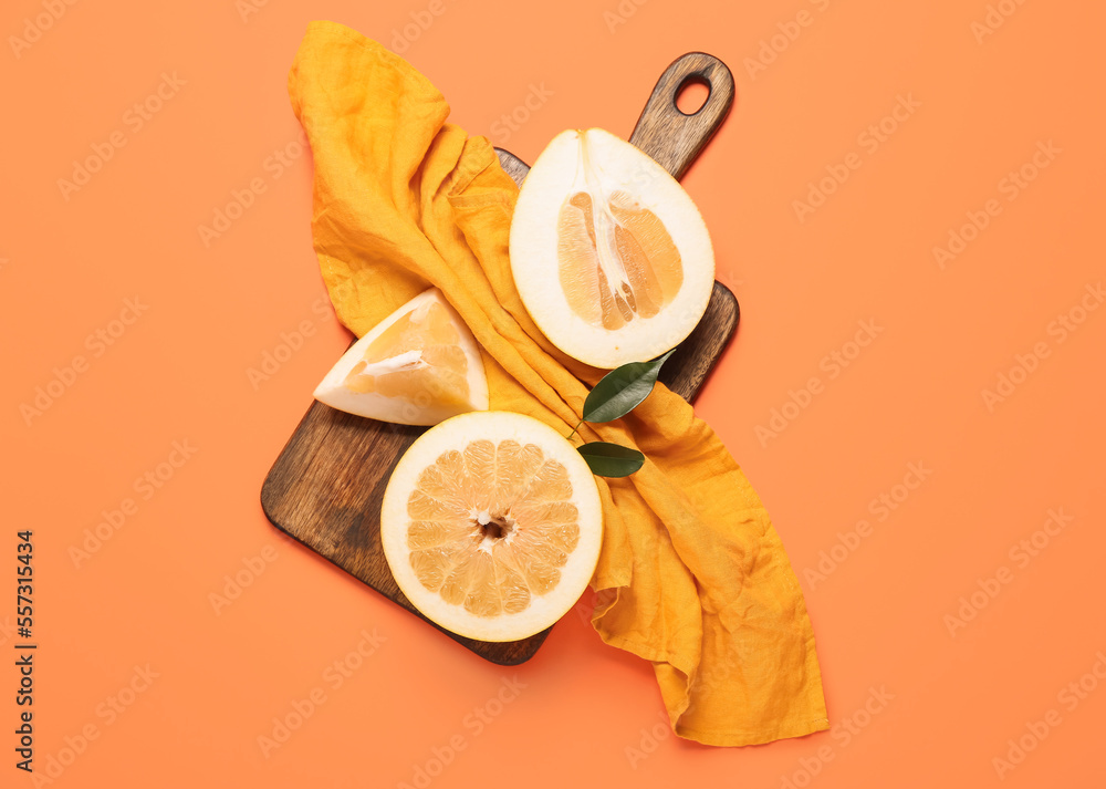 Cutting board with pomelo halves and kitchen towel on orange background