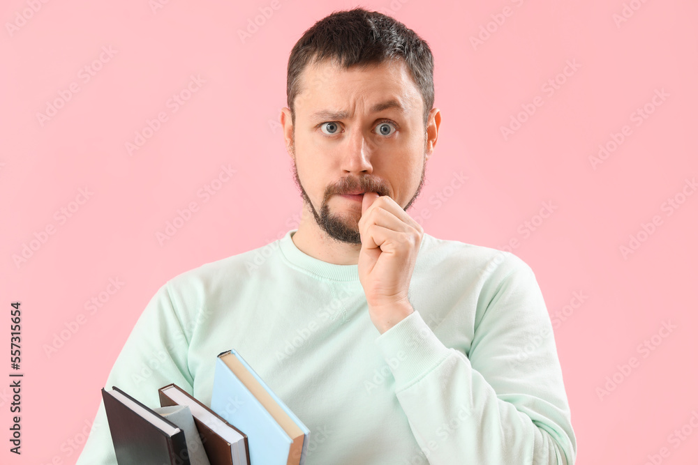 Handsome man with books biting nails on pink background