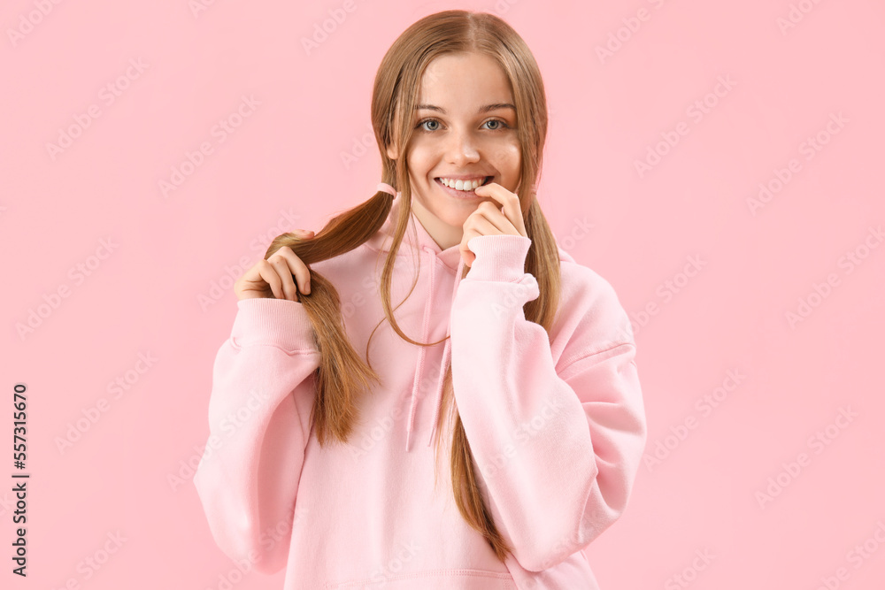 Young woman in hoodie biting nails on pink background