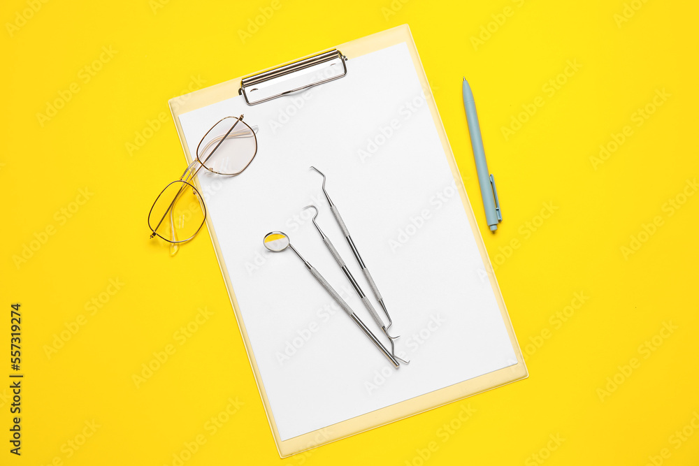 Clipboard with dental tools, eyeglasses and pen on yellow background