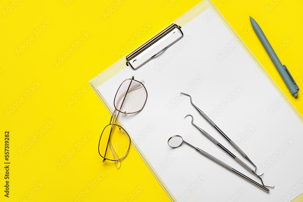 Clipboard with dental tools, eyeglasses and pen on yellow background