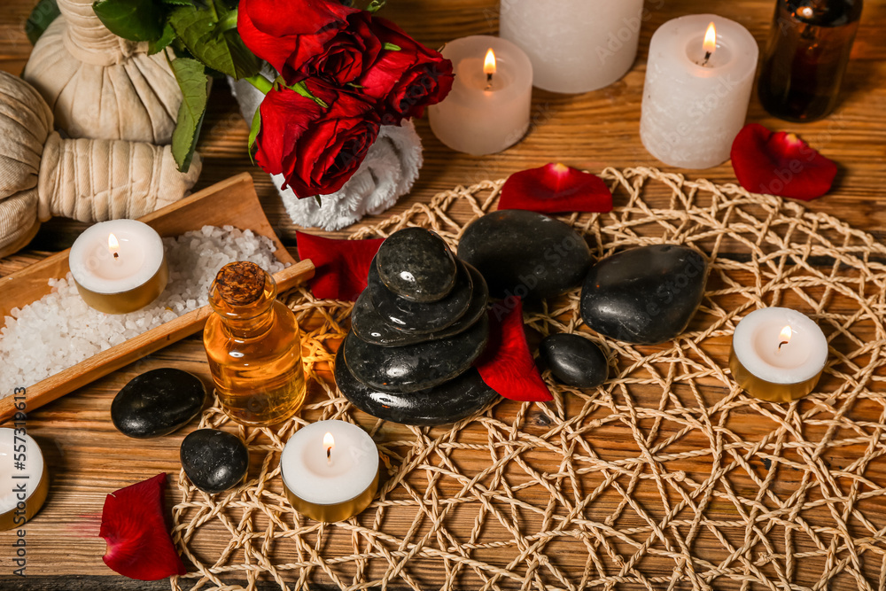 Spa stones with burning candles and roses on wooden table, closeup. Valentines Day celebration