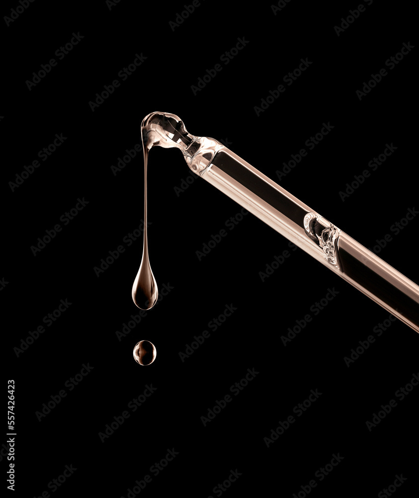 Drops dripping down from cosmetic pipette closeup on a black background