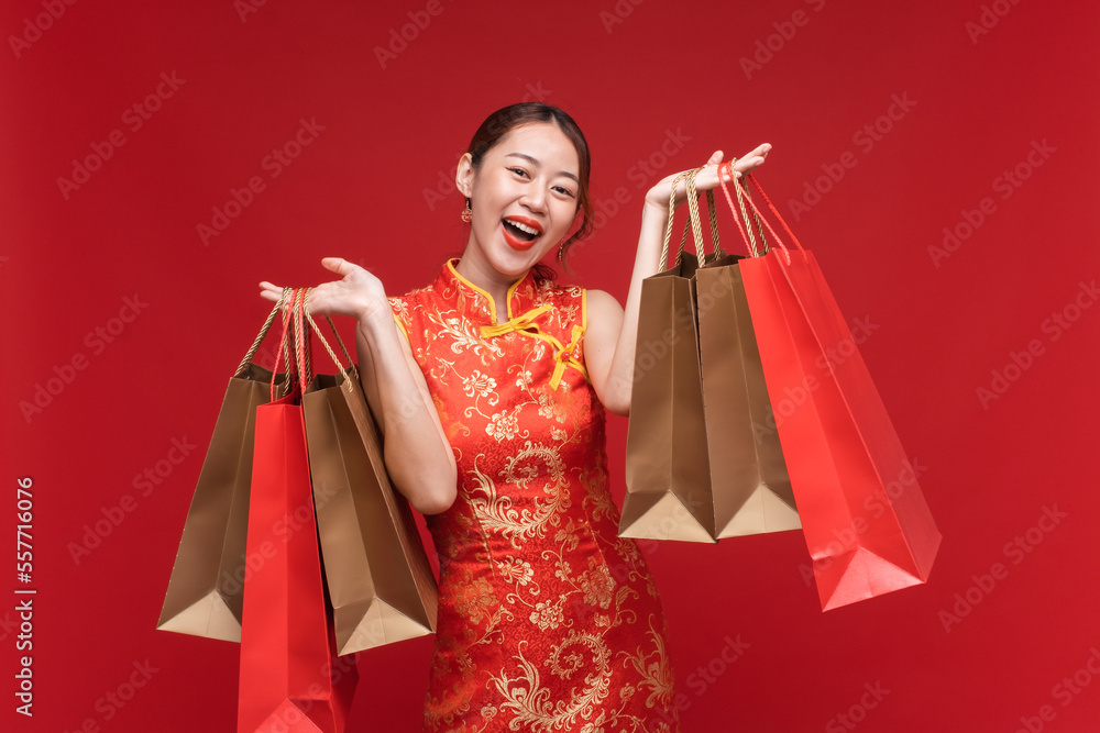 Young asian woman wearing qipao cheongsam dress with shopping bags on red background for Chinese new