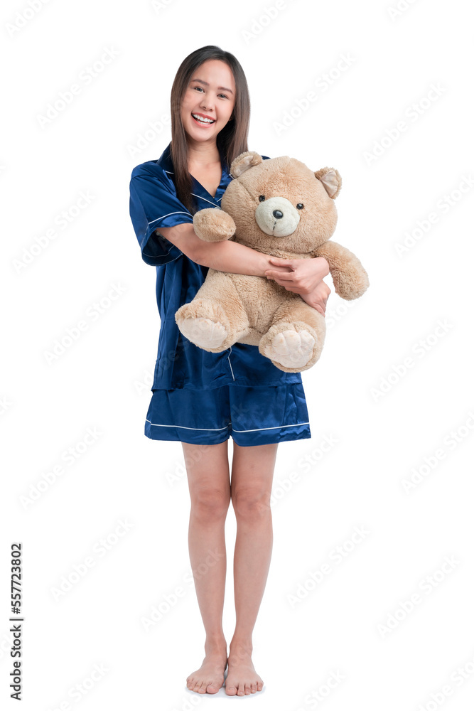 Young asian teen woman with cosy sleep wear hugging teddy bear stuffed animal with happy face smilin