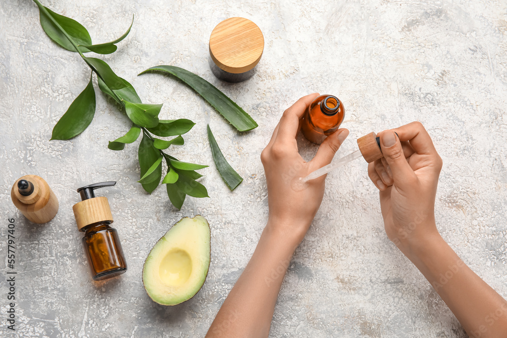 Young woman applying essential oil onto hand on light background