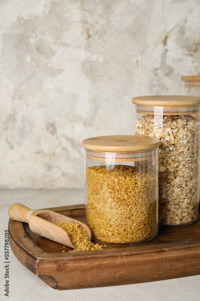 Wooden board with jars of cereals on light table, closeup