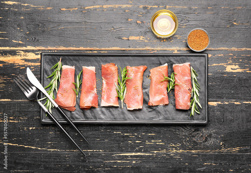 Plate with slices of tasty ham, rosemary, mustard seeds and oil on dark wooden background