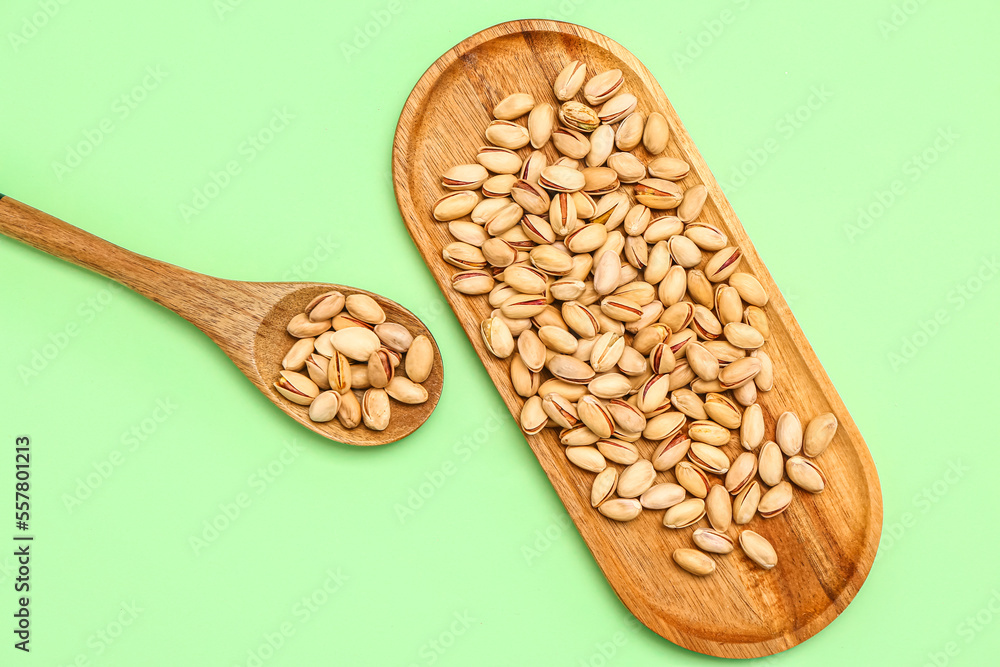 Cutting board and spoon with tasty pistachio nuts on green background