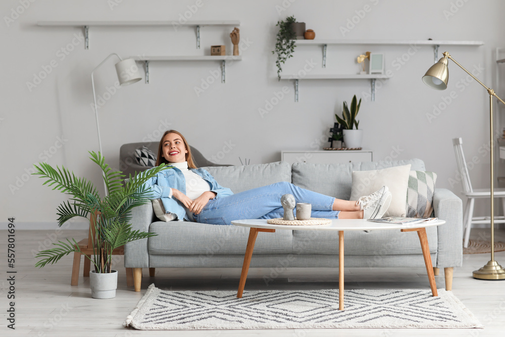 Young woman lying on grey couch at home