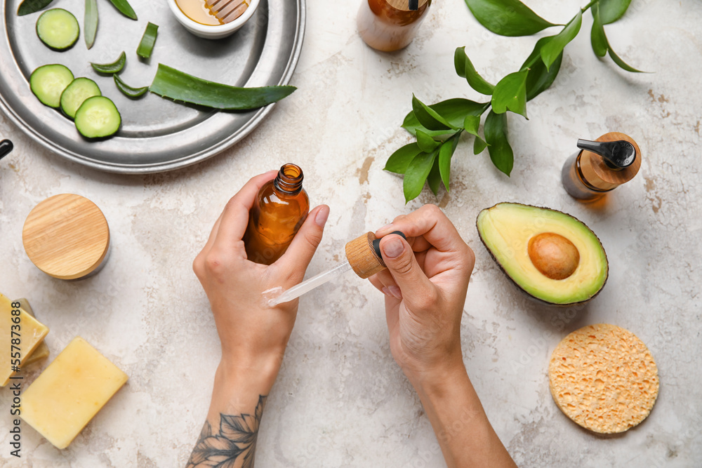 Woman applying essential oil onto hand on light background