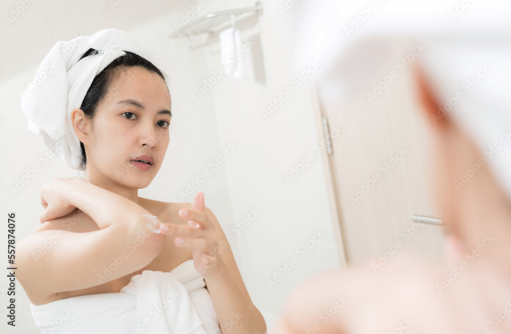 Happy young Asian woman applying lotions on her body in bathroom