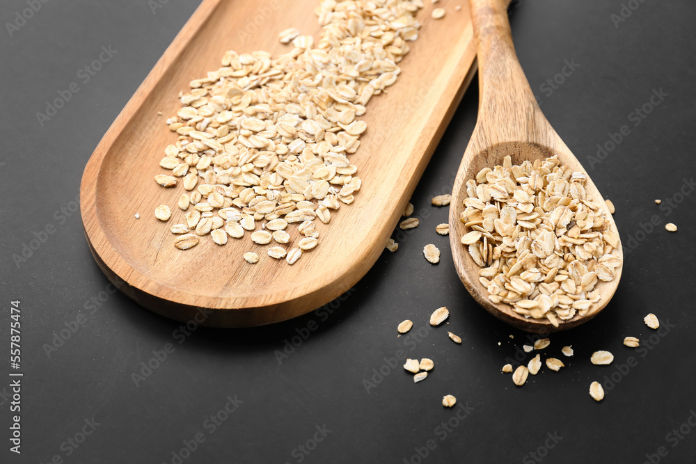 Wooden board and spoon with raw oatmeal on dark background, closeup