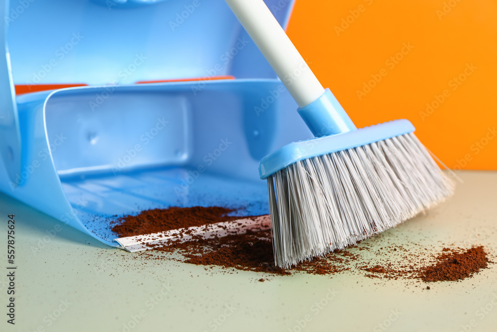 Cleaning of scattered coffee with dustpan and broom on color background, closeup