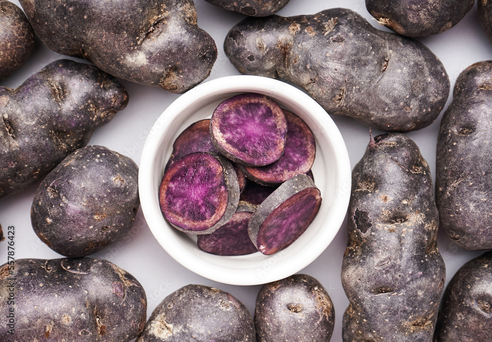 Bowl with cut and whole purple potatoes on white background, closeup