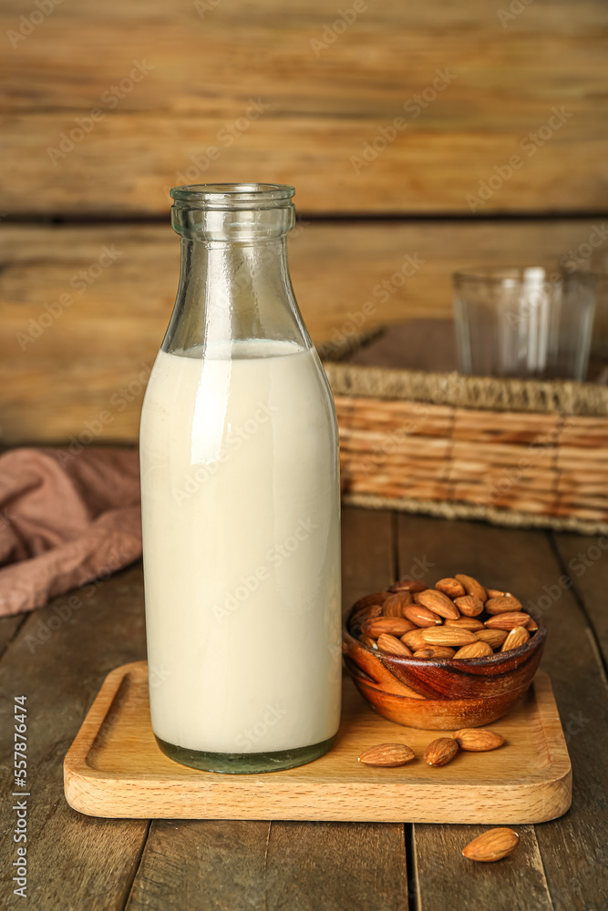 Board with bottle of almond milk and nuts on wooden table