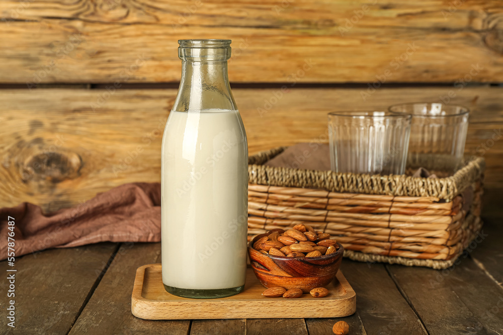 Board with bottle of almond milk and nuts on wooden table