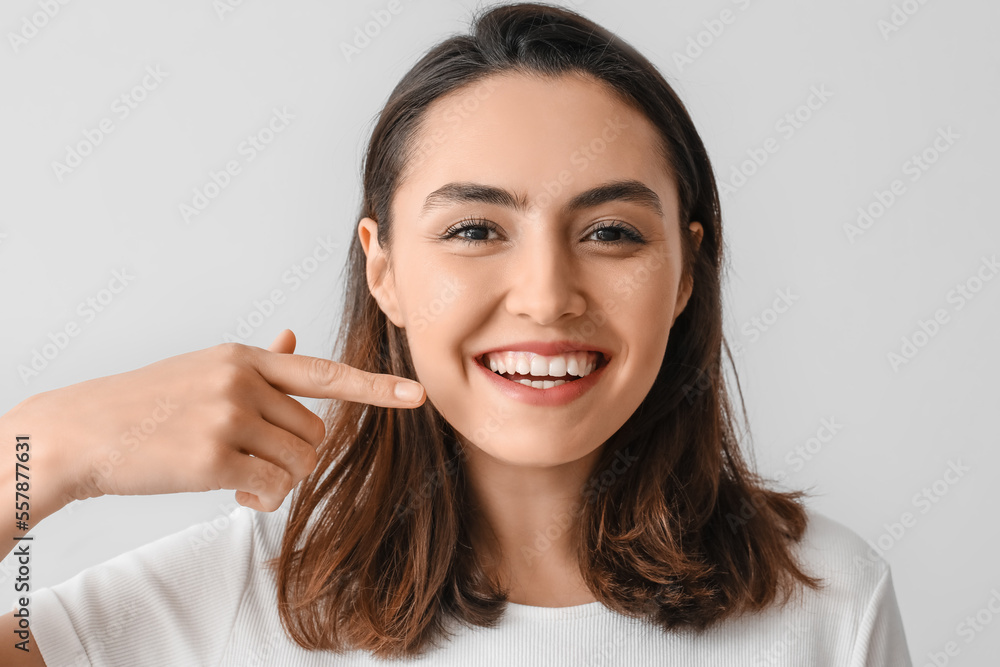 Young woman pointing at her teeth on grey background, closeup