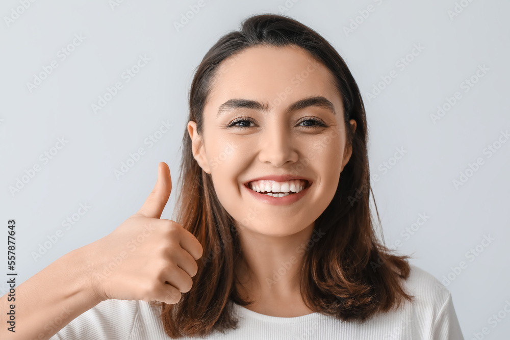 Young woman with beautiful smile showing thumb-up on grey background, closeup