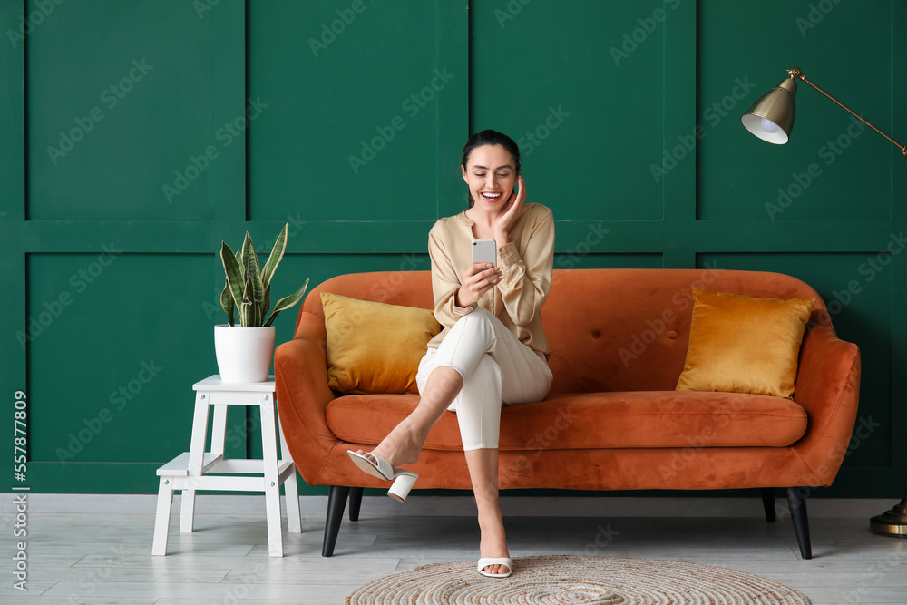 Young woman using mobile phone on red sofa near green wall