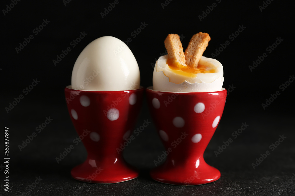 Holders with soft boiled eggs and croutons on black background