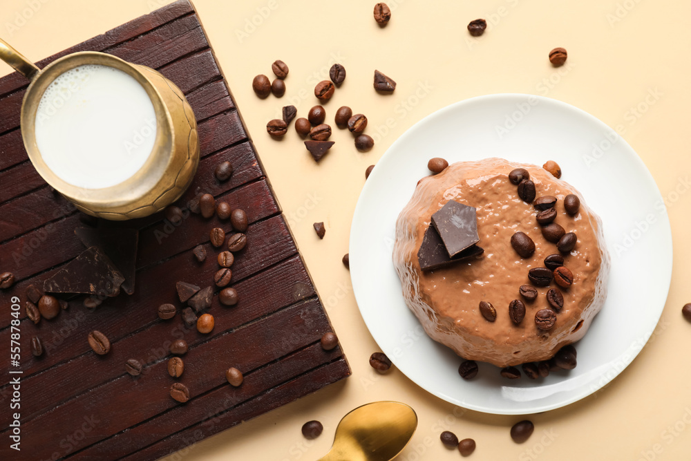 Plate with delicious pudding, coffee beans, chocolate, board and cup of milk on beige background