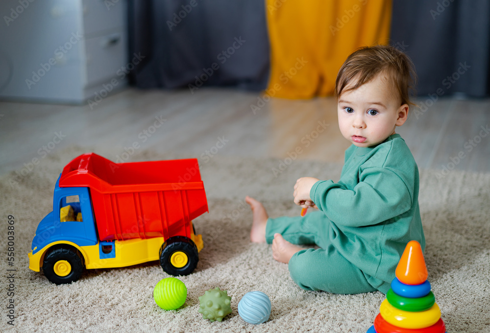 Cute cheerful baby playing with colorful toy at home. Toddler boy with toy lorry. Child with educati