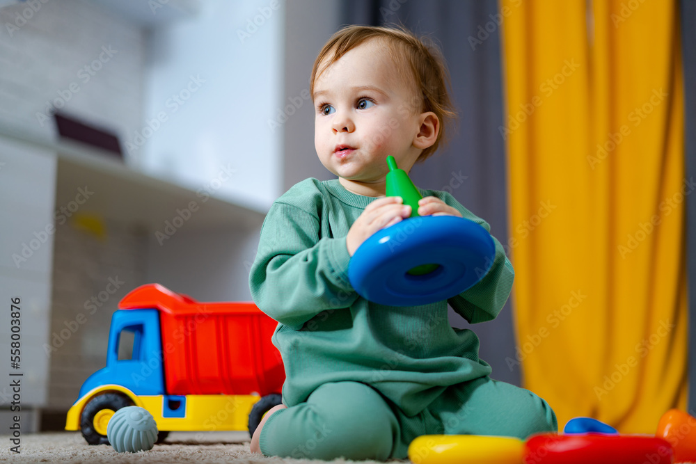 Baby boy playing with his colorful toys on floor at home. Child with educational toy. Early developm