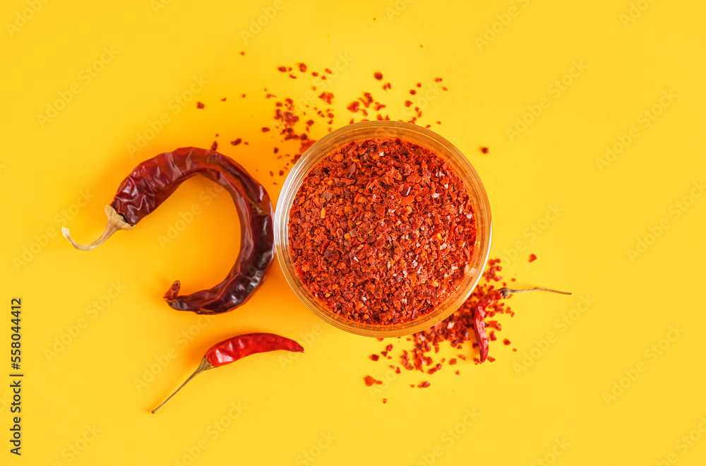 Bowl of chipotle chili flakes on color background