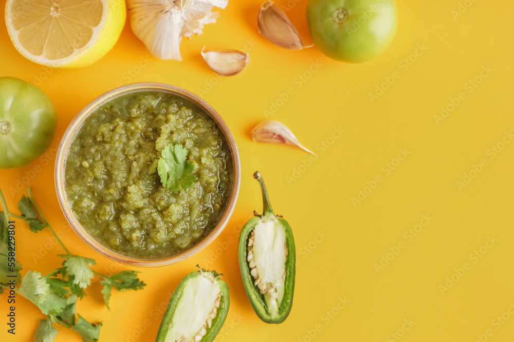 Composition with bowl of tasty green salsa sauce and ingredients on yellow background