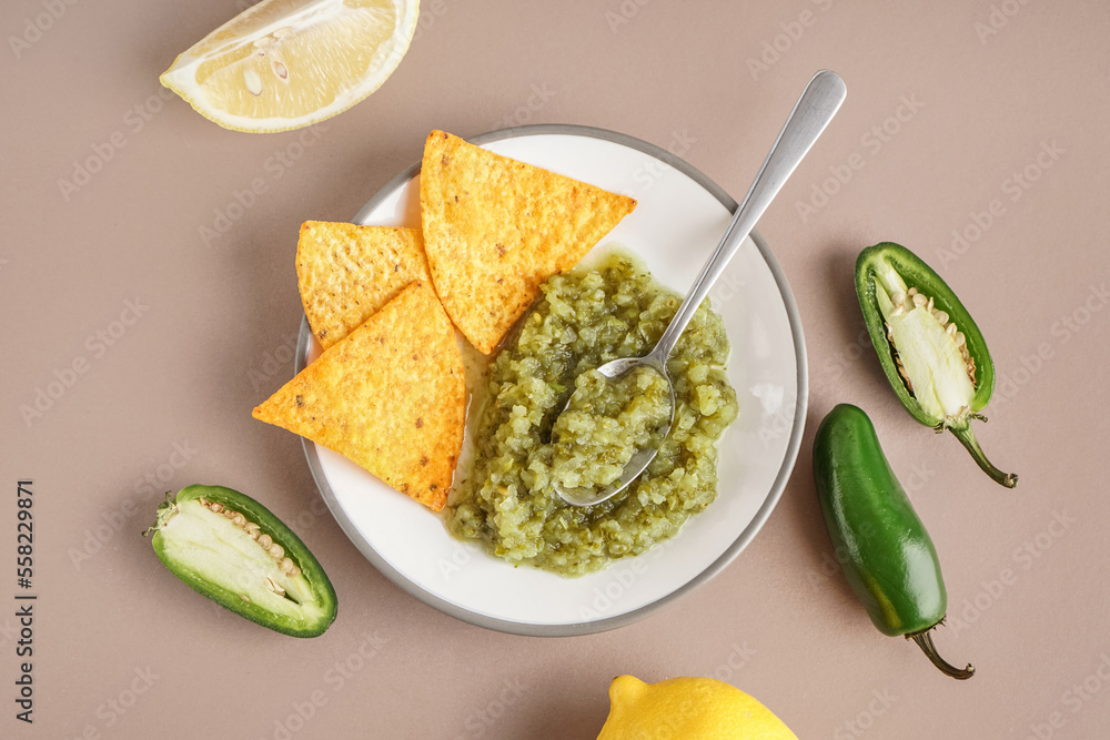 Plate of tasty green salsa sauce with nachos on color background