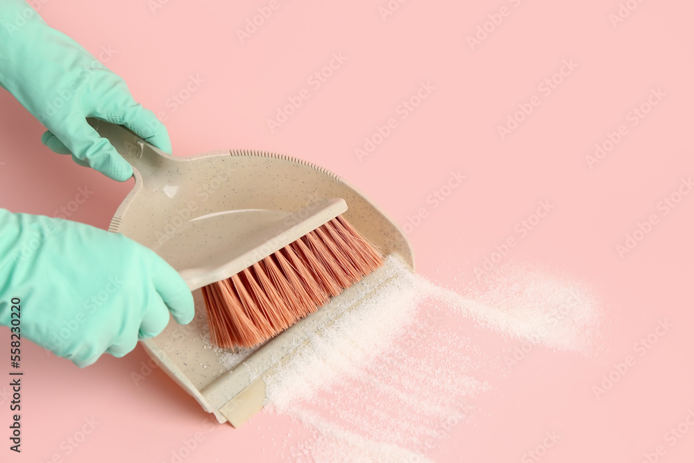 Woman in rubber gloves sweeping sugar with dustpan and brush on pink background