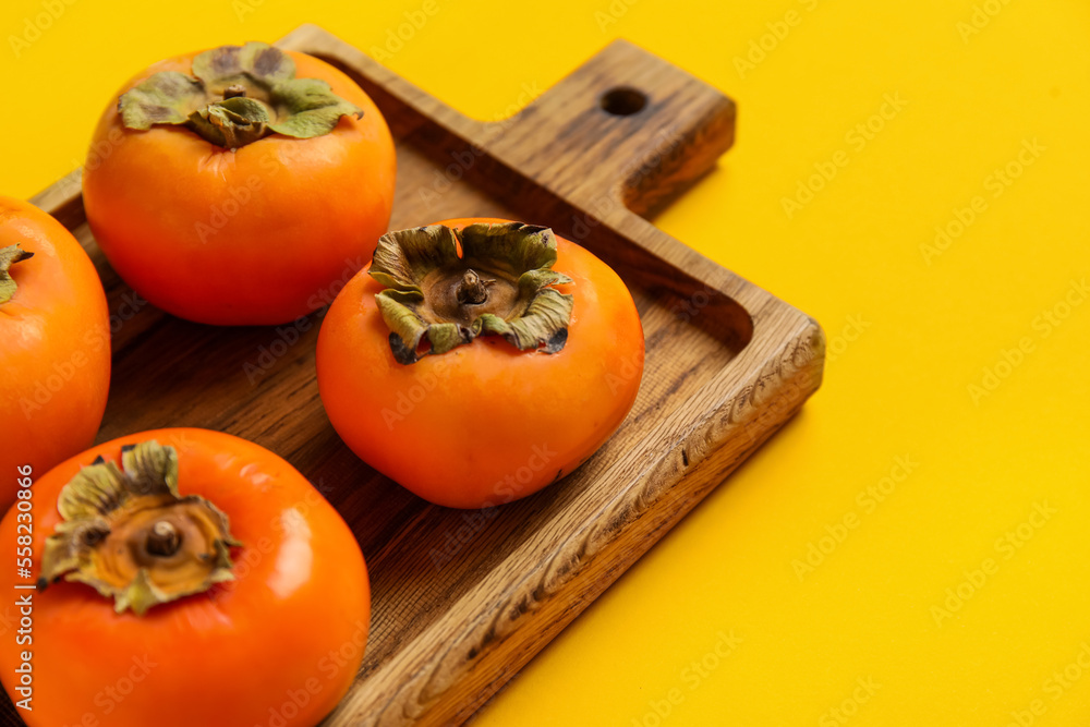 Wooden board with fresh ripe persimmons on color background, closeup