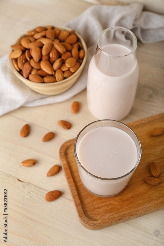 Board with glass, bottle of almond milk and nuts on wooden background