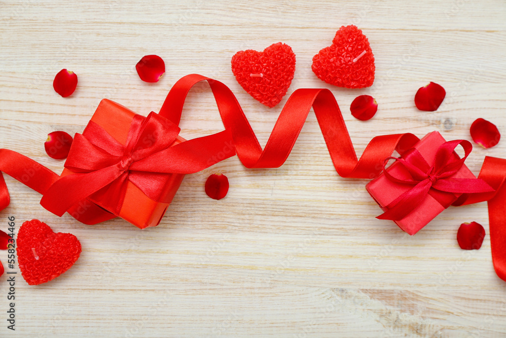 Gifts with ribbon, candles and rose petals on light wooden background. Valentines Day celebration