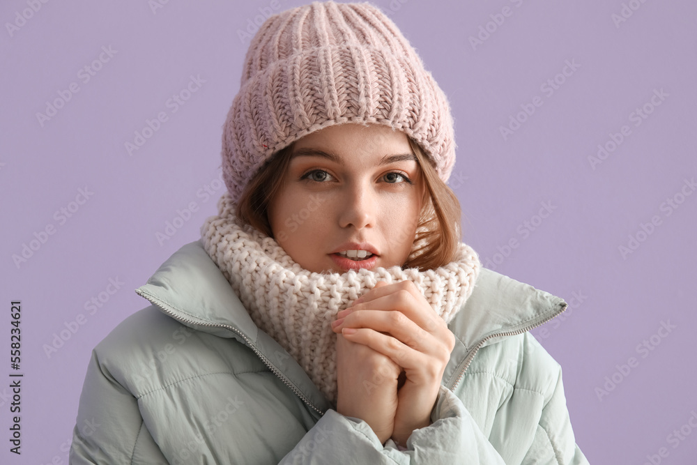 Frozen young woman in winter clothes on lilac background, closeup