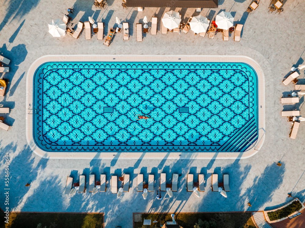 Young attractive woman swims on the back in the swimming pool, lady holds her arms up, flecks in the